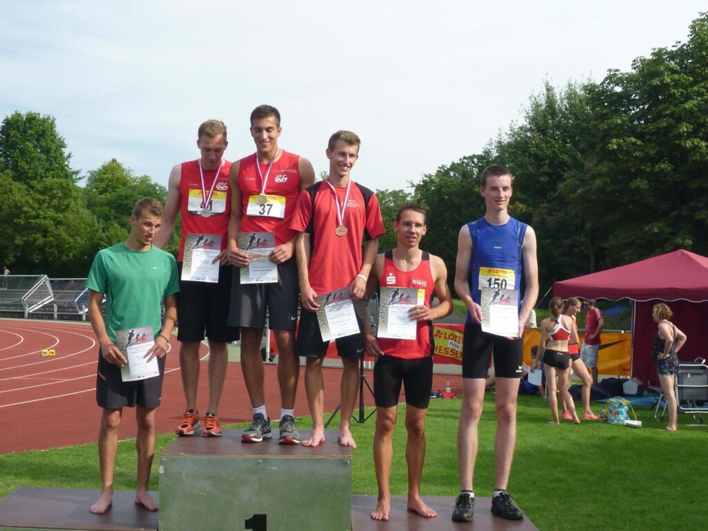 Sechs Leichtathleten bei der Siegerehrung auf dem Podest, mit Medaillen und Urkunden, zwei davon im roten Trikot des asc Darmstadt